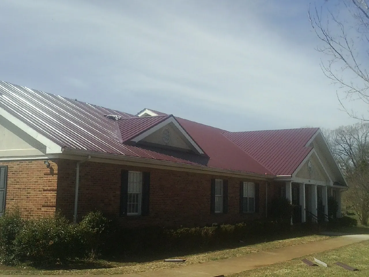 Red metal roof with gabled entries on a long brick building, from a Hail Damage Roof Repair job in Elkton