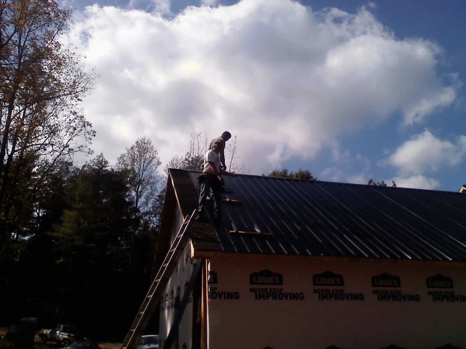 Roofer fastening dark metal panels high against a cloudy sky, from a Roof Inspection job in Elkton